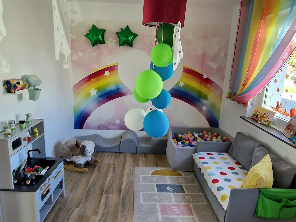 Gruppenraum mit Bällebad, Sofa, Spielküche und Regenbogen-Wandbild