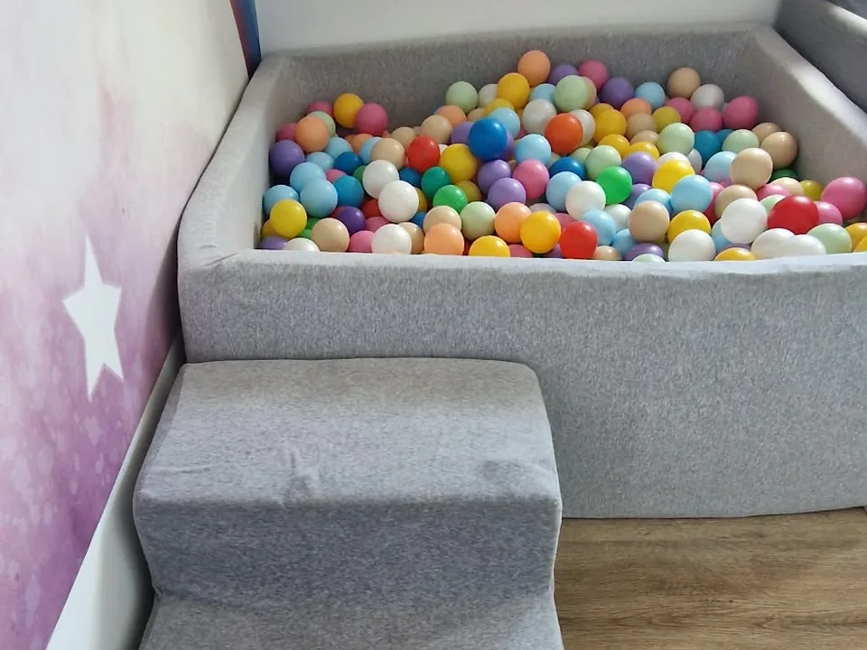 Bällebad mit bunten Bällen und Schaumstoffstufen vor einer Wand mit Stern- und Regenbogenmotiv