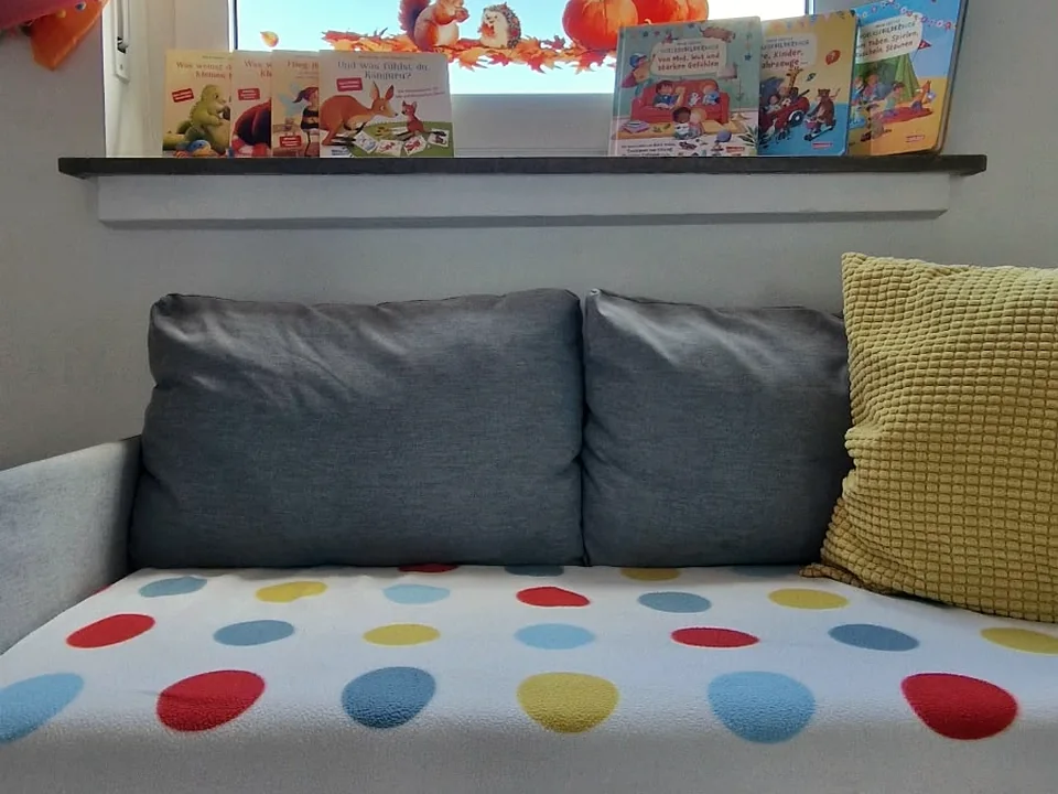 Gemütliches Sofa mit Kinderbüchern und buntem Vorhang am Fenster