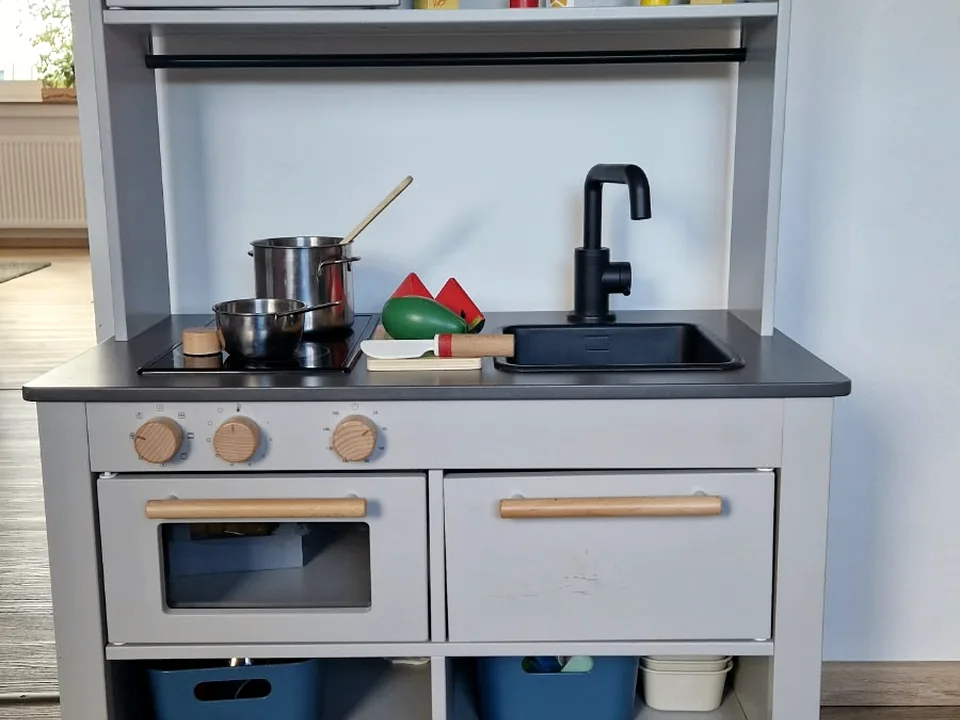 Kinderküche mit kleinen Töpfen, Spiellebensmitteln und Holzarmaturen